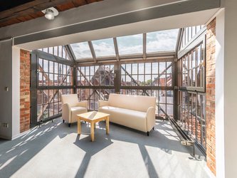 komplett verglaste Loggia im Dachgeschoss mit weißem Sofa und Sessel