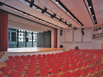 Saal mit vielen roten Stühlen vor einer Bühne